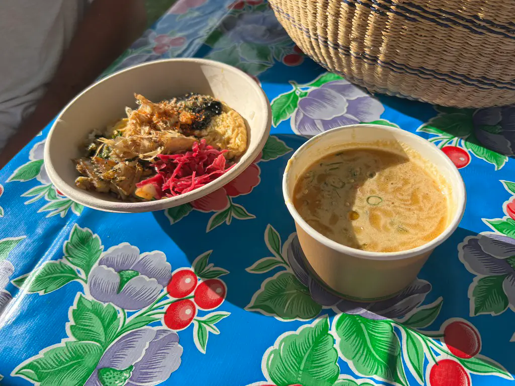 A Japanese breakfast donburi topped with bonito flakes and pink pickles, with a cup of soup, on a floral tablecloth at the Ohayo Japanese Brekky market stall