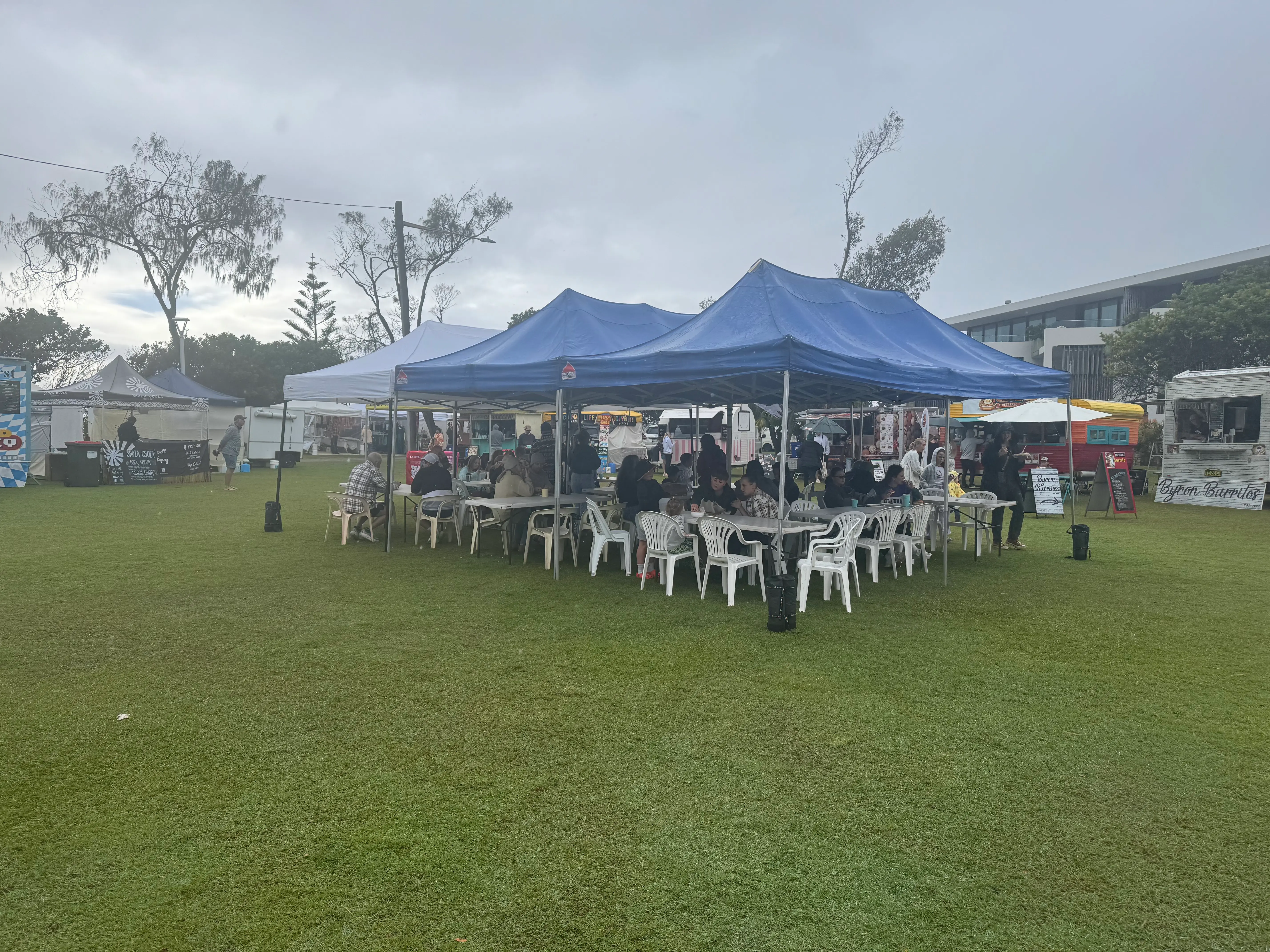 A grey-weather view of Byron Community Market stalls and people moving through the market