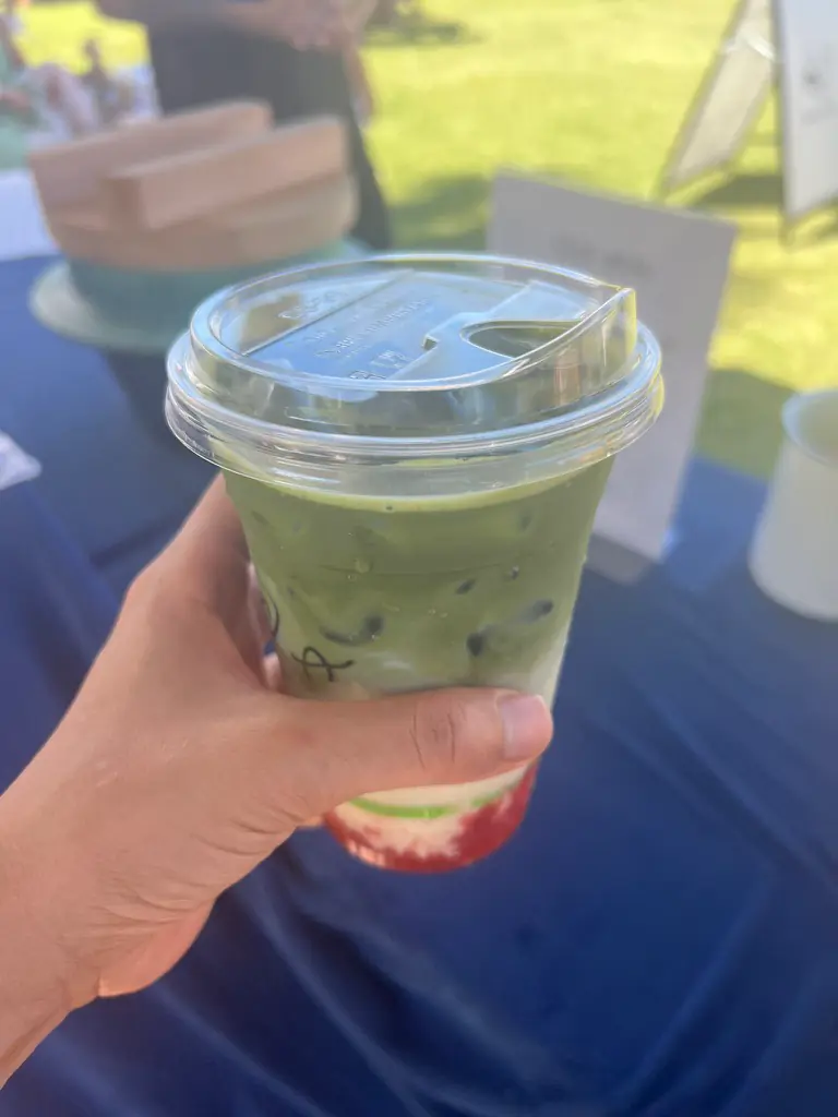 A hand holding an iced matcha latte with a layer of strawberry at the bottom at the Byron Bay Farmers Market