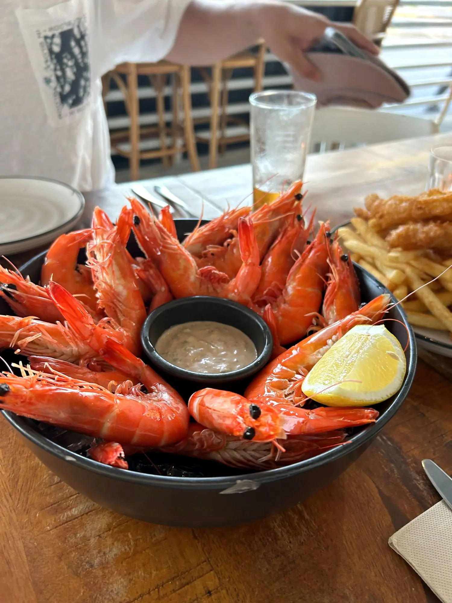 A bowl of cooked local prawns with a lemon wedge and aioli, chips in the background