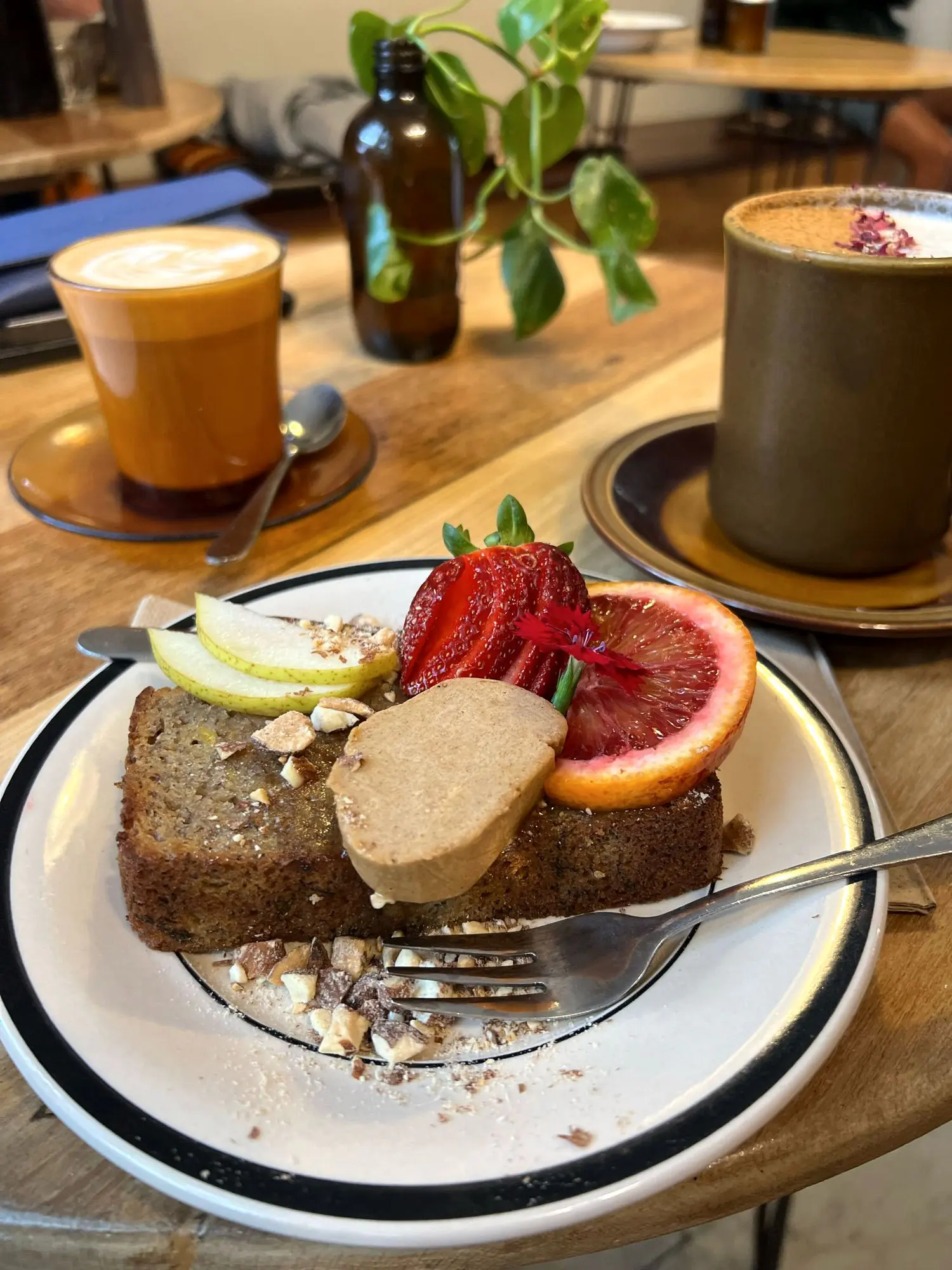 A plate of banana bread topped with seasonal fruit and nuts beside two coffees at Folk Byron Bay