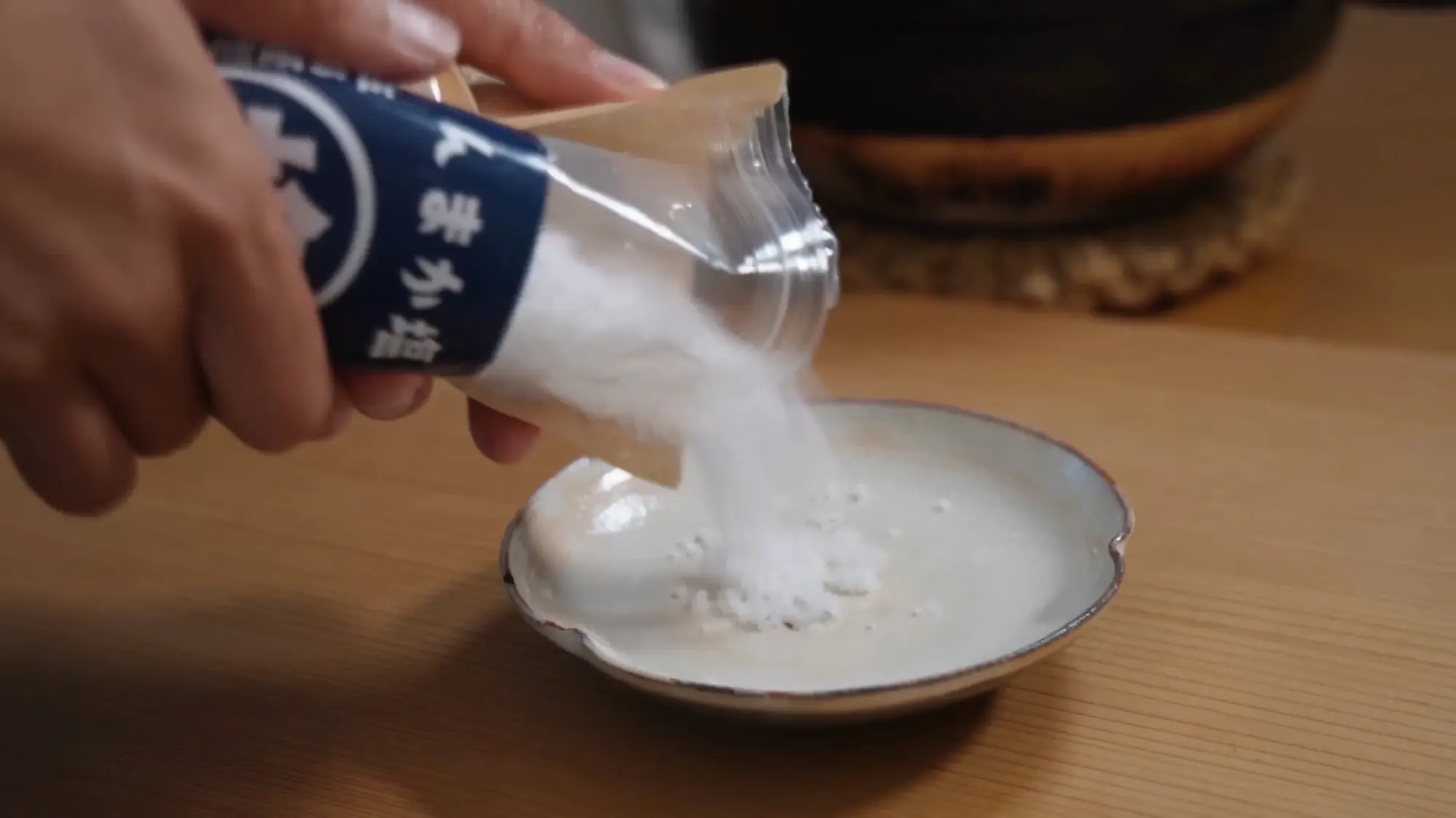 Coarse white sea salt being poured from its bag into a small ceramic dish